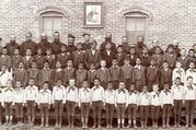 Jesuits and boys under picture of St. Ignatius at the Holy Rosary Mission circa 1880-1900. Courtesy of Marquette University, Raynor Memorial Libraries and Holy Rosary Mission – Red Cloud Indian School Records, ID: MUA_HRM_RCIS_02937.