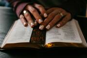 A woman rests her hands on the open pages of a Bible.