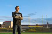 Joe Kennedy standing with crossed arms in front of a football field.