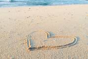 A heart drawn in the sand next to the water on a beach.