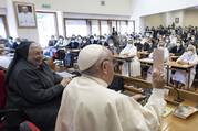 A smiling religious sister in habit sits to the left of Pope Francis before a crowd of sisters