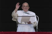 Pope Francis stands at a podium, waving towards the camera
