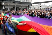 people standing around a large pride flag of many colors in belgium in may 2018