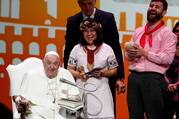 Pope Francis, seated, smiles as he speaks into a microphone, flanked by a laughing man and woman