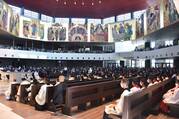 people sitting in a church with paintings on the wall. the people closest to the camera are seminarians or priests