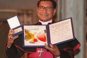 bishop belo of dili, east timor, holds his nobel peace prize in a 1996 photo, he wears his bishops' clothes with a purple hat and belt