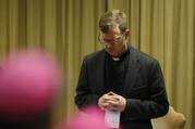 A man in a Roman collar bows his head in prayer