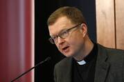 A priest in a Roman collar speaks into a microphone