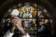 Rome, Italy: on the foreground, the priest is holding the host in the hands. On the background, stained-glass window in the church of Santa Croce in Gerusalemme built between the 3rd and the 4rd c.. The current look of the church was made in the 18th c.