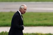 king charles walks wearing a dark suit with green grass behind him