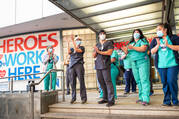 health care workers clapping outside a hospital wearing masks during covid, there is a sign behind them denoting them as heroes