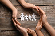  ‌Photo of three sets of hands encircling four attached paper dolls, one of a father, one of a mother, and two of children. (iStock/Liudmila Chernetska)