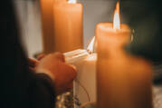 A closeup of a couple's hands as they light church candles (iStock/Wirestock)