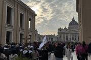 pilgrims make their way toward st peters basilica under a cloudy sky
