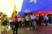 Opposition members wave a Venezuelan flag outside a poll station during a symbolic referendum in Caracas, Venezuela, on July 16. Venezuela's opposition called for a massive turnout Sunday in a symbolic rejection of President Nicolas Maduro's plan to rewrite the constitution, a proposal that's escalating tensions in a nation stricken by widespread shortages and more than 100 days of anti-government protests. (AP Photo/Ariana Cubillos)