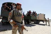 Member of Iraqi security forces stands guard in front of army volunteers. (CNS photo/Ahmed Saad, Reuters)