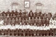 Jesuits and boys under picture of St. Ignatius at the Holy Rosary Mission circa 1880-1900. Courtesy of Marquette University, Raynor Memorial Libraries and Holy Rosary Mission – Red Cloud Indian School Records, ID: MUA_HRM_RCIS_02937.