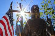 an american flag stands to the left next to a crucifix with light coming from behind it, a bronze statue of Jesus is to the right