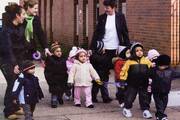 Three women smile at each other while walking with a group of small toddlers.