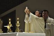man holds up the eucharist at an altar with candles in front of him