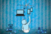 a child reaches up to a cot mobile with computers and phones hanging from it