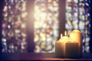 candles sit in front of a stained glass window with light streaming through it