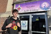 a student from kolbe academy stands at the front door of the school which has a sign with the school's name on it