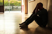 a young man in shadow sits with his head in his hands in an empty hallway