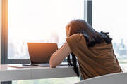 A stressed student with her head in her hands sitting in front of a laptop computer 