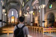 a young man wearing a backpack stands in the back of a church