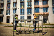 Two boys stand on a swing set in front of a modern, mid-rise apartment building.