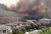A brushfire on a hill threatens a row of single-family homes, below, in Southern California. (iStock/f00sion)