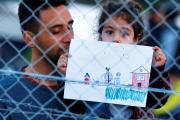 FENCED IN. A young refugee girl holds up a drawing in a makeshift camp on the Macedonian-Greek border, November 2015. 