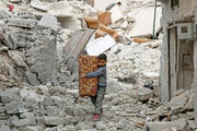 CITY IN RUINS. A young boy of Aleppo emerges from the rubble with what little he could salvage after an Assad regime attack in November.