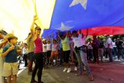 Opposition members wave a Venezuelan flag outside a poll station during a symbolic referendum in Caracas, Venezuela, on July 16. Venezuela's opposition called for a massive turnout Sunday in a symbolic rejection of President Nicolas Maduro's plan to rewrite the constitution, a proposal that's escalating tensions in a nation stricken by widespread shortages and more than 100 days of anti-government protests. (AP Photo/Ariana Cubillos)
