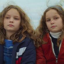 An image from the film Petite Maman of two sisters sitting next to each other in winter jackets