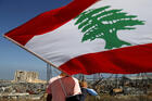 A man holds the Lebanese flag, as he looks at the scene of Tuesday's explosion that hit the seaport of Beirut, Lebanon, Friday, Aug. 7, 2020. Rescue teams were still searching the rubble of Beirut's port for bodies on Friday, nearly three days after a massive explosion sent a wave of destruction through Lebanon's capital. (AP Photo/Hussein Malla)