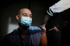 a bald, masked man receives a vaccination in the arm, his sleeve rolled up