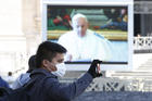 A man wearing a mask takes a photo as Pope Francis appears on a video monitor in St. Peter's Square as he leads the Angelus from his library in the Apostolic Palace at the Vatican March 8, 2020. (CNS photo/Paul Haring)