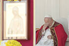 Pope Francis, seated and dressed in red priests clothing, covers his eyes 