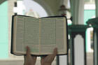 A woman holds aloft an opened copy of the Quran in a prayer space.