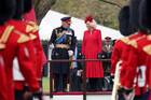 king charles in full regalia walks next to queen camilla who wears red with some british soldiers and guard in front of them