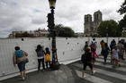 Tourists peer through protection panels securing a perimeter around the Notre Dame Cathedral ahead of the start of a massive lead decontamination in Paris, Thursday, Aug. 15, 2019. (AP Photo/Francois Mori)