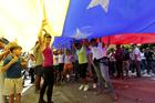 Opposition members wave a Venezuelan flag outside a poll station during a symbolic referendum in Caracas, Venezuela, on July 16. Venezuela's opposition called for a massive turnout Sunday in a symbolic rejection of President Nicolas Maduro's plan to rewrite the constitution, a proposal that's escalating tensions in a nation stricken by widespread shortages and more than 100 days of anti-government protests. (AP Photo/Ariana Cubillos)